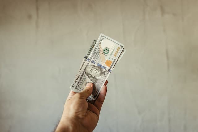 a hand holding one hundred dollar bills
