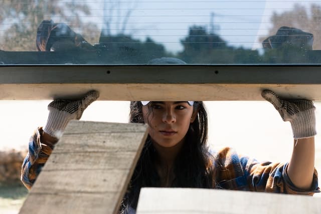 holding up a window while wearing a plaid shirt and baseball hat
