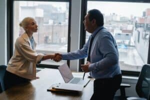 two people in an office wearing suits and shaking hands over a table