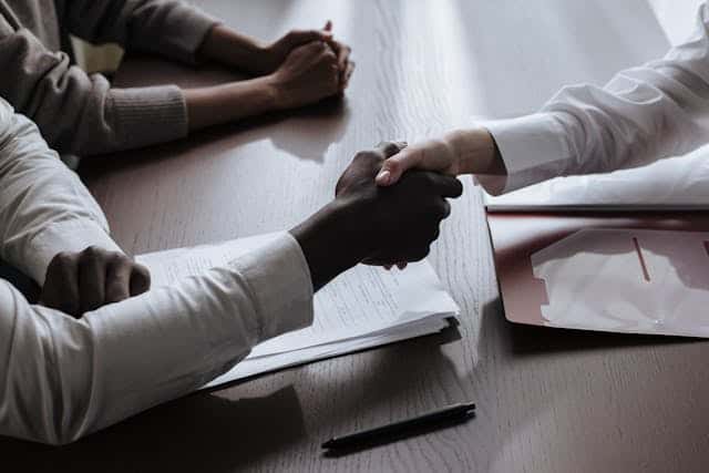 two-people-shaking-hands-over-a-contract-on-a-desk